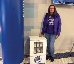 Founder of Steps of Hope Iowa Ann Breeding poses with one of many Narcan distribution stations her organization helped bring to campus.