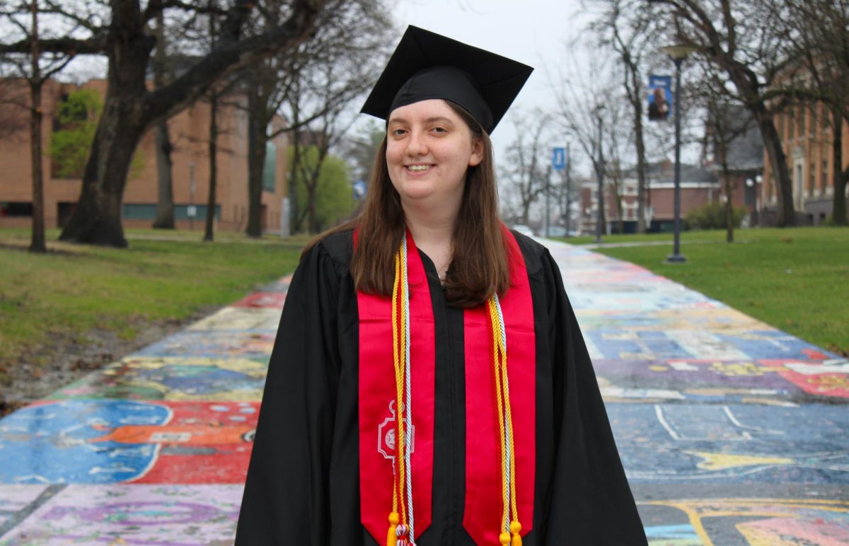 Editor-in-chief Lily Wasserman stands in front of Painted Street in her graduation gown. Wasserman believes people should apply the principles of journalism to their everyday lives.